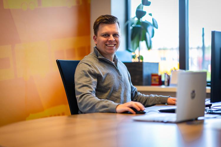 Een kantoormedewerker zit achter zijn laptop en glimlacht
